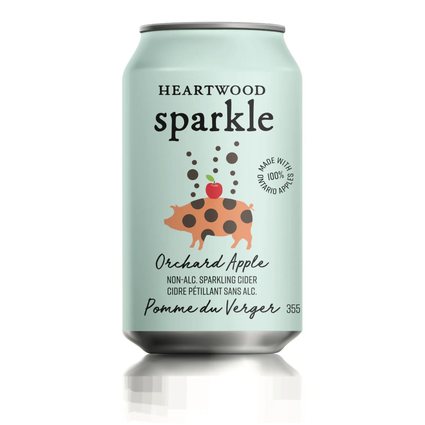 A mint-green aluminum can labeled “HEARTWOOD Sparkle Orchard Apple” is displayed against a plain white background. The design is clean and modern, with black text and a playful illustration. Brown bubbles float above a stylized orange pig with dark spots, balancing a red apple with a green leaf. A circular stamp reads “MADE WITH 100% ONTARIO APPLES.” The lower text describes it as non-alcoholic sparkling cider, with French translation and “355” indicating volume.