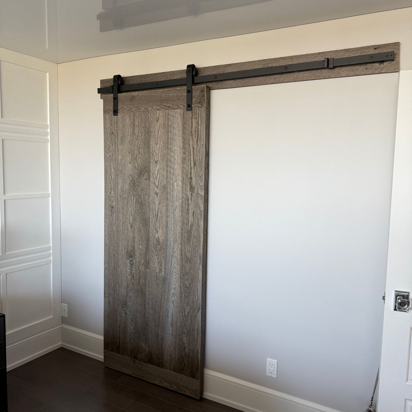 Harvest grey hemlock sliding barn door with matte black cast iron track installed in a modern interior by Milano Woodworking.