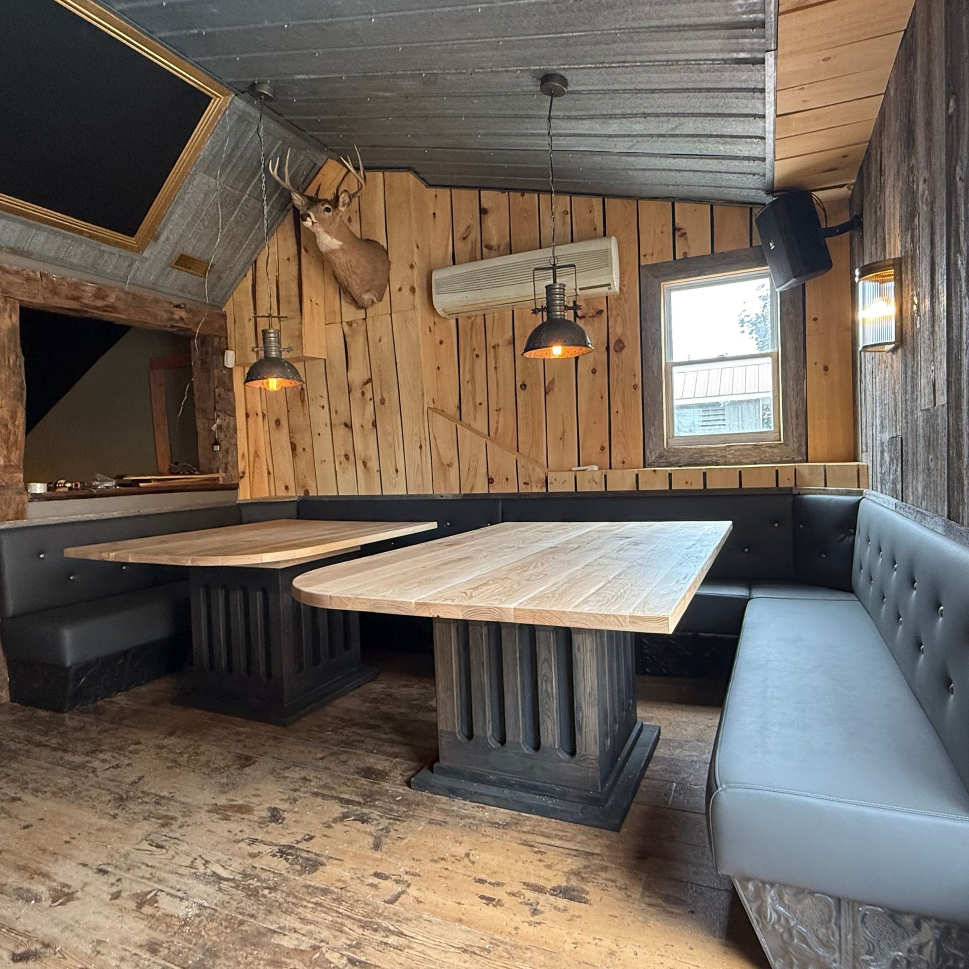 Handcrafted white ash dining tables with matte finish and black-stained bases installed in a rustic dining space by Milano Woodworking.