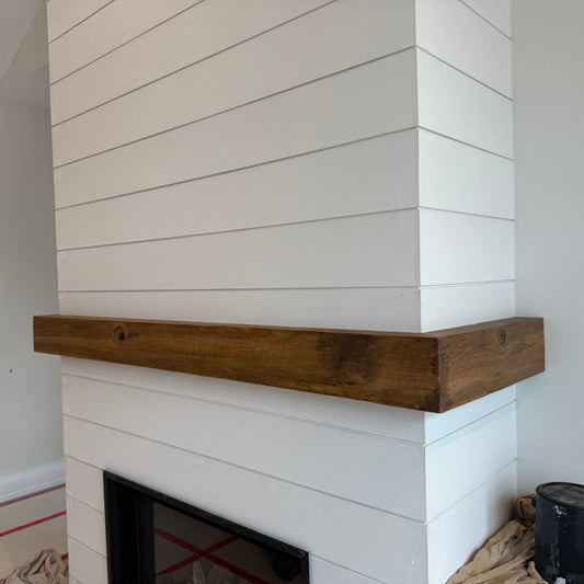 Handcrafted mantle made from reclaimed brown barn board installed on a white shiplap fireplace surround by Milano Woodworking.