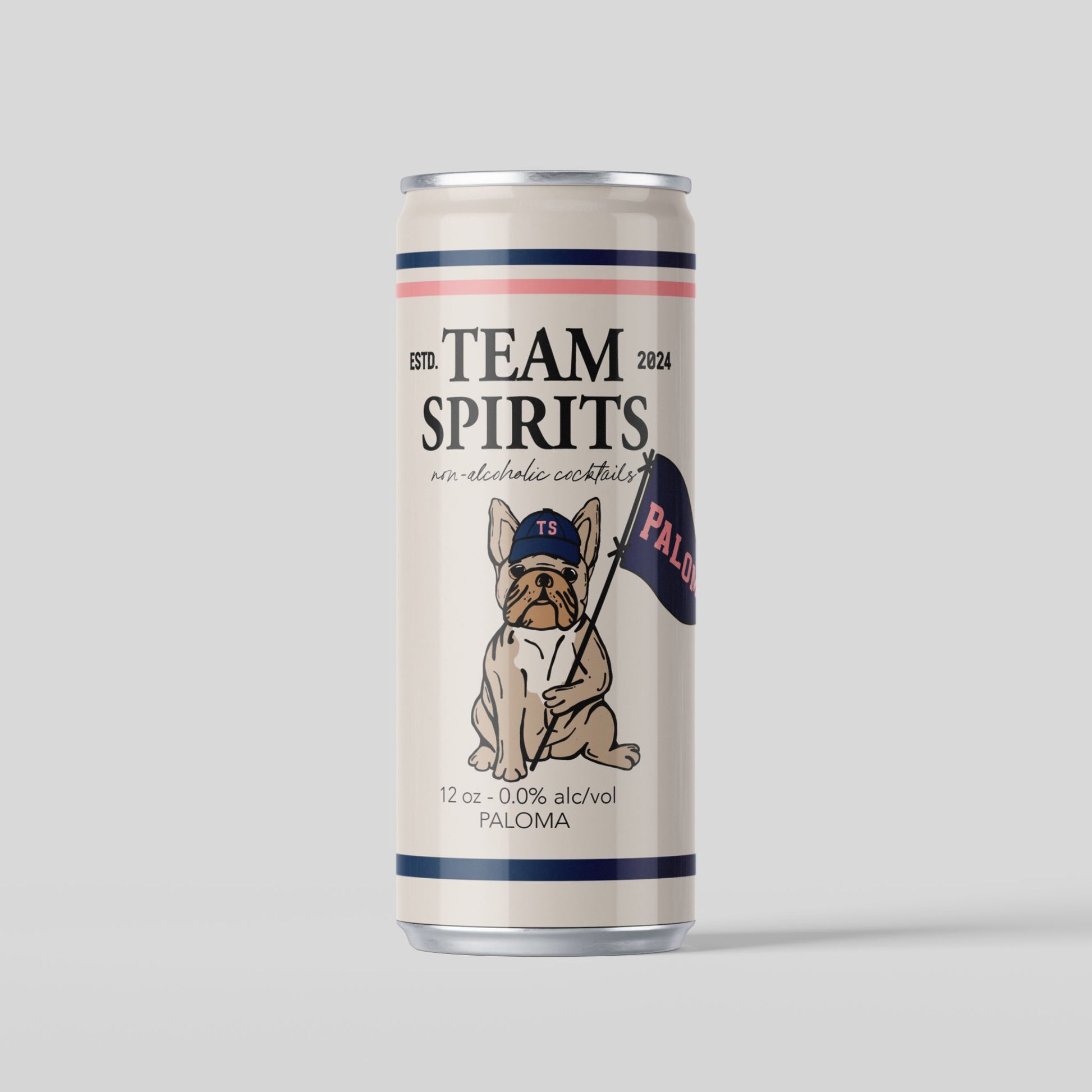 A cream-colored can of Team Spirits non-alcoholic Paloma. The can has dark blue and light pink horizontal stripes at the top and bottom. The center of the can features an illustration of a bulldog wearing a blue baseball cap and holding a flag that says "PALOMA". The text "TEAM SPIRITS" is at the top of the can, with "non-alcoholic cocktails" below it. The can also specifies "12 oz - 0.0% alc/vol" and "PALOMA" at the bottom. The background is a solid light gray.