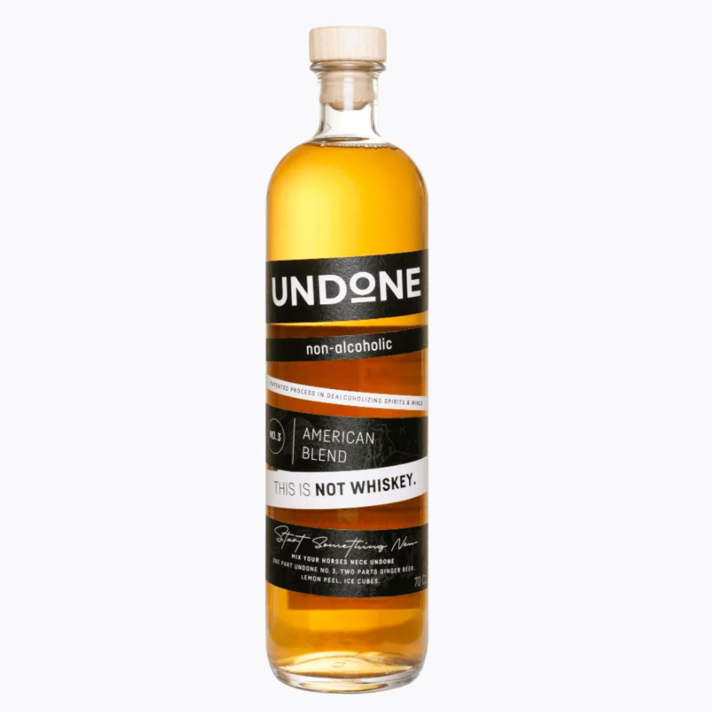 A full-length, centered shot of a clear glass bottle of UNDONE non-alcoholic American Blend is presented against a bright white background. The non-alcoholic spirit has a rich, amber-gold color, visible through the glass. The bottle is sealed with a simple wooden or cork stopper. The primary label is a striking black and white design with an orange-brown accent stripe. The brand name "UNDONE" is at the top in large white text on black. Below this, it is clearly identified as "non-alcoholic." The center of t