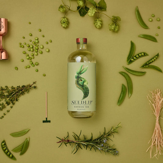 A photo of a 700 milliliter bottle of Seedlip Garden 108 Herbal surrounded by herbs. Seedlip is available for sale at knyota.com