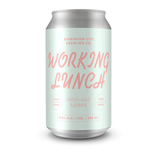A close-up image of a silver beverage can featuring a light mint green label. The label reads "DOMINION CITY BREWING CO." in pink at the top, and "WORKING LUNCH" in a larger, stylized pink font below. Further down, it says "NON-ALC LAGER" in pink, with "CLEAN" and "CLEAR" on the left and "BEER" and "BIÈRE" on the right, all in smaller pink text within dashed circles. At the bottom of the label, "0.5% ALC. / VOL. | 355 mL" is printed. The background is a clean white, emphasizing the can.