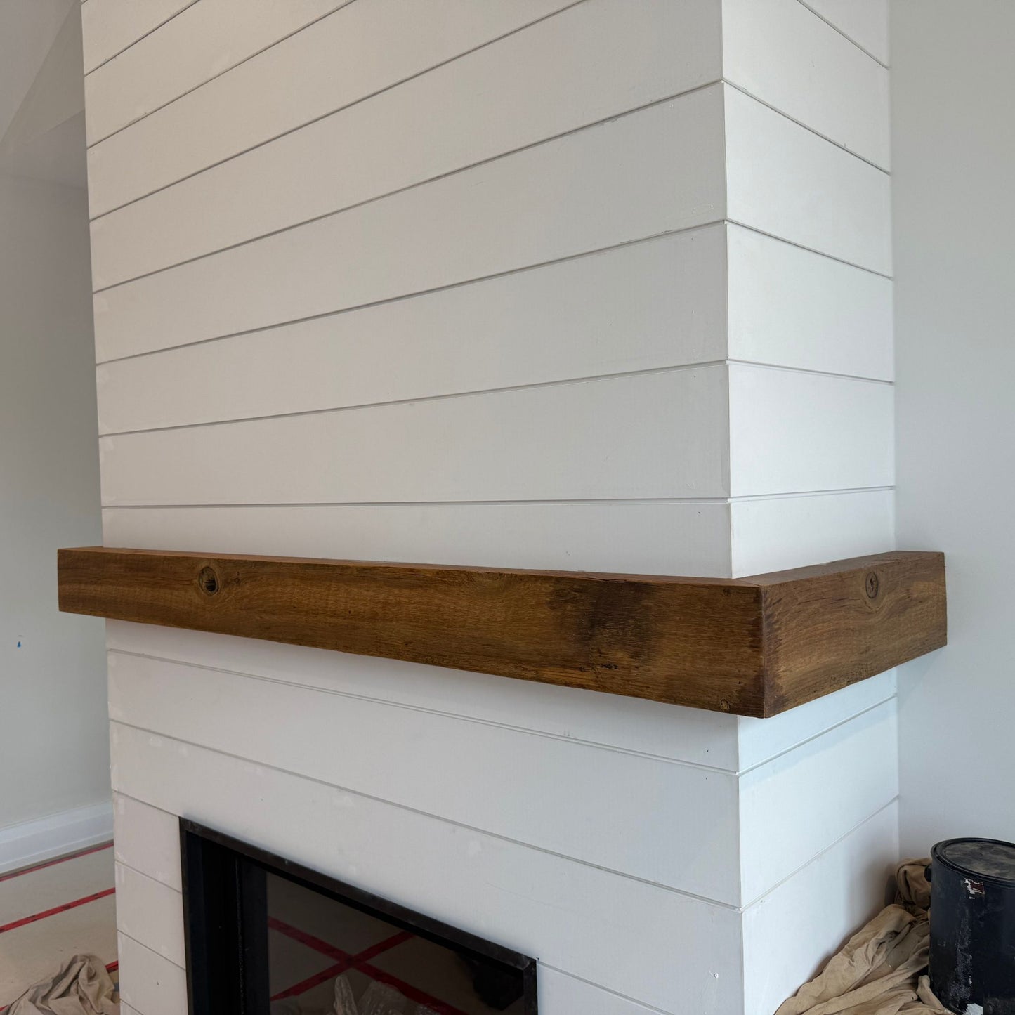 Handcrafted mantle made from reclaimed brown barn board installed on a white shiplap fireplace surround by Milano Woodworking.