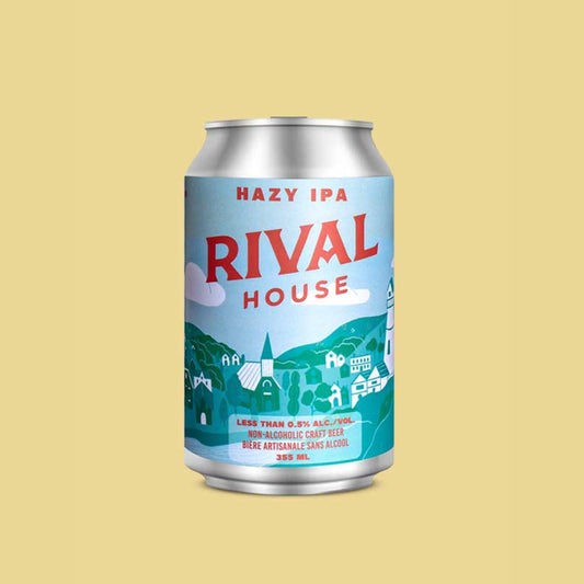 A silver can of Rival House Hazy IPA against a pale yellow background. The can's label is light blue and features a whimsical, light-toned village scene with buildings and a lighthouse. "RIVAL HOUSE" is printed in large red letters at the top, and "HAZY IPA" is written in red above it. The bottom of the label has text that reads "LESS THAN 0.5% ALC./VOL. NON-ALCOHOLIC CRAFT BEER" and "BIÈRE ARTISANALE SANS ALCOOL" along with "355 ML".