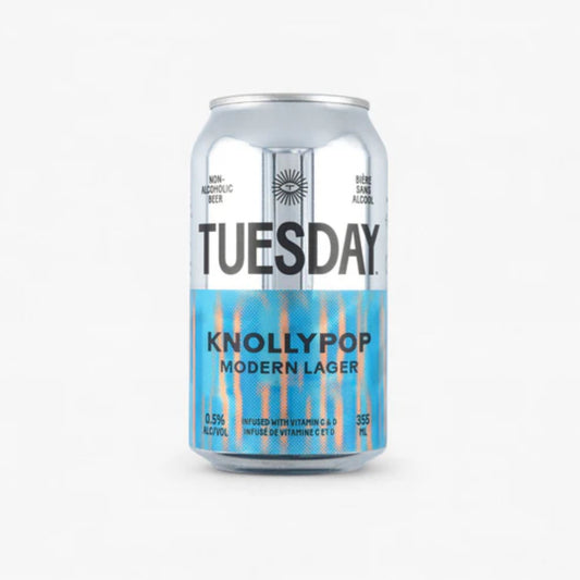 The image shows a silver can of Tuesday Knollypop Modern Non-Alcoholic Lager. The can has a black label with the brand name "Tuesday" in large white letters. The can is labeled as non-alcoholic beer with 0.5% alcohol by volume. It is also infused with vitamins C and D.